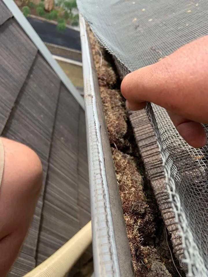 Packed debris and silt underneath gutter guard — completely blocking the gutter